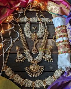 an assortment of necklaces and bracelets are displayed on a wooden surface with lights in the background