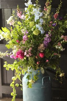 a large blue vase filled with lots of flowers sitting on top of a table next to a wooden door