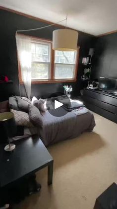 a bedroom with black walls and carpeted flooring has a bed, dressers, tv, and window