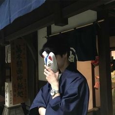 a man in a blue kimono is holding something up to his face