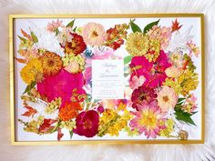 an arrangement of flowers is displayed in a gold frame on a white furnishing