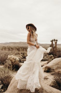 a woman standing on top of a rock in the desert wearing a dress and hat