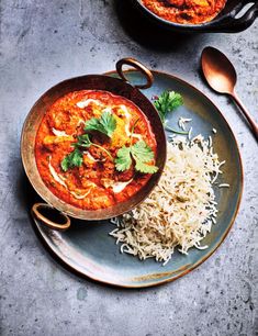 two bowls of food on a plate with spoons next to one bowl filled with rice