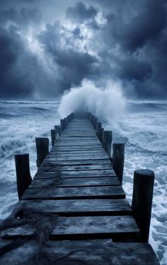 a pier with waves crashing over it and dark clouds in the sky above, as seen from the ocean