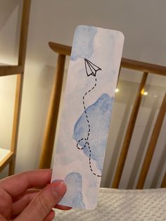 someone holding up a bookmark with a paper airplane drawn on it and a string attached to it