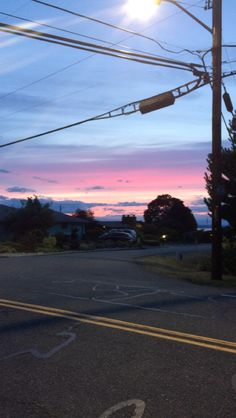 the sun is setting behind power lines and telephone poles in an empty street with no cars on it