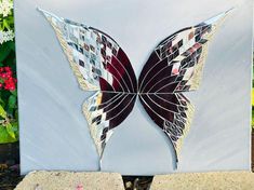 a butterfly made out of stained glass sitting on top of cement blocks in front of flowers