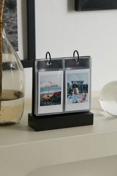 two photos are placed on a black and white photo holder next to a glass vase