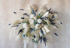 a bouquet of white flowers and blue feathers on a wooden stand against a wall with no one around it