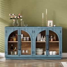 a blue cabinet with glass doors and shelves filled with bottles, glasses, vases and other items