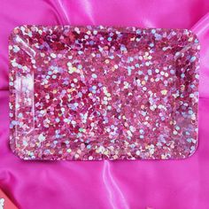 a pink tray with some confetti in it on a pink satin material background