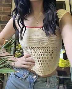 a woman with long black hair wearing a crochet top and jeans, holding a plant