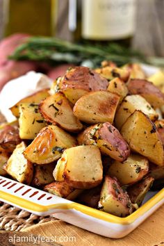 potatoes with herbs in a yellow and white dish on a wicker place mat next to wine bottles