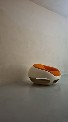 an orange and white chair sitting on top of a cement floor next to a wall