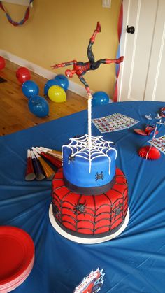 a spiderman themed birthday cake on a blue tablecloth with balloons and streamers