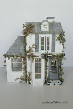 a doll house with ivy growing on the roof and windows, in front of a white wall