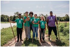 a group of people standing next to each other in front of a river holding shovels