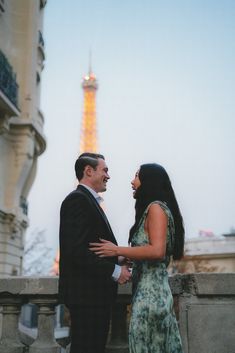 a man and woman standing next to each other in front of the eiffel tower