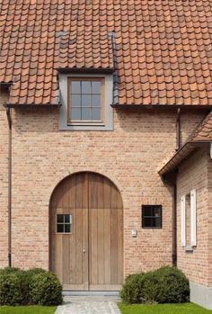 a brick house with an arched wooden door and brown tile on the roof is shown