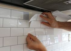 two hands on a white tile wall and one hand holding a roll of toilet paper