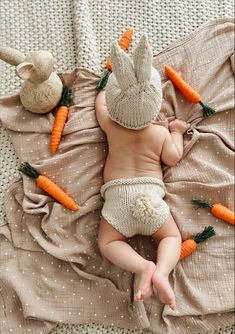 a baby wearing a bunny hat and diaper laying on a bed with carrots