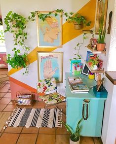 a living room filled with lots of plants and pictures on the wall above a desk