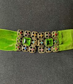 This is a quite lovely little belt from the 1930s.  It is made from a vibrant acid or apple green velvet that is nearly 1.5 inches (3.5cm) wide.  The closure is a rectangular buckle made up of 2 squares which are in turn made up of 9 small squares.  8 of these mini squares is made of etched and punched brass with a different coloured glass stone in the centre.  The ninth (middle) square is a large single emerald cut apple green glass stone.  The closure between each half is a hook.  The buckle i Adjustable Belt With Antique Buckle For Party, Vintage Adjustable Belt For Party, Vintage Adjustable Belts For Formal Wear, Adjustable Vintage Party Belt, Luxury Vintage Green Cuff Bracelet, Green Victorian Multi-stone Jewelry, Vintage Adjustable Turquoise Belt, Vintage Adjustable Multicolor Belts, Vintage Green Rhinestone Brooch