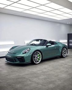 a green sports car is parked in a large room with concrete flooring and white walls