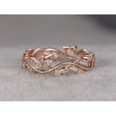 a rose gold wedding band with diamonds on the sides and leaves in the middle, sitting on top of a white cloth