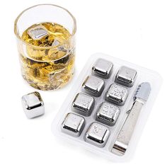 an ice cube tray with four pieces of silver and two glasses of whiskey on the side