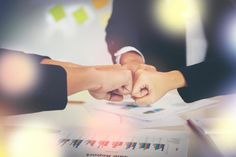 two people holding hands while sitting at a desk in front of papers and paperwork on top of a table