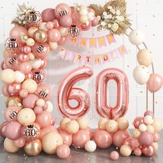 a pink and white balloon arch with the number sixty in front of it, surrounded by balloons