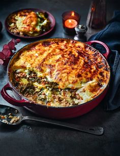 a casserole dish with meat and vegetables in it on a table next to candles