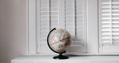 a small globe sitting on top of a white shelf in front of shuttered windows