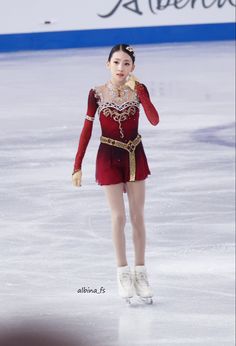 a female figure skating on the ice in a red dress with gold trimmings