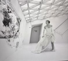 a black and white photo of a woman in a dress walking through a room with an open door