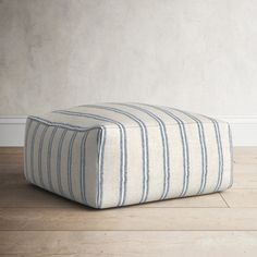 a striped ottoman sits on the floor in front of a white wall and wooden floors