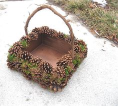 a basket filled with lots of pine cones sitting on top of snow covered ground next to grass