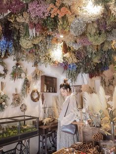 a woman standing in front of a table filled with dried flowers and wreaths hanging from the ceiling