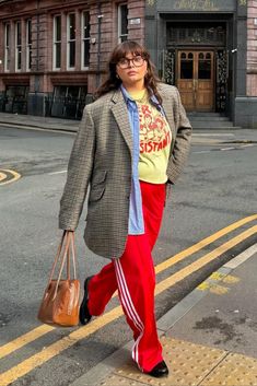 a woman is walking down the street carrying a handbag in her right hand and looking at the camera