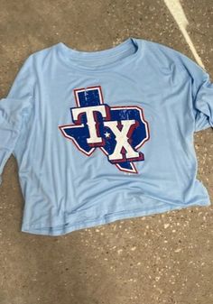 Texas Rangers Womens Alt Cap T-Shirt - Light Blue Trendy Blue T-shirt For Fall, Blue Stretch Tops With Letter Print, Oversized Spring College Tops, Spring Oversized Tops For College, Stretch Letter Print Top For College, Blue Spring College Tops, Casual Tops For College In Spring, Blue Pre-shrunk Tops For Spring, Blue Tops With Text Print For Spring