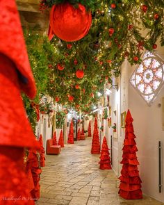 a hallway decorated for christmas with red decorations and ornaments hanging from the ceiling, surrounded by greenery