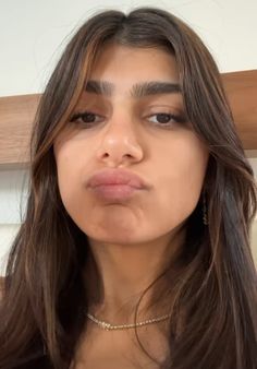 a woman with long brown hair wearing a choker and looking at the camera while making a funny face