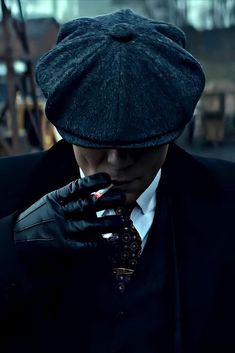 a man in a suit and hat is holding his hand to his face while wearing gloves