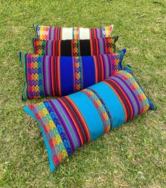 three colorful pillows sitting on top of a lush green field next to a pillow case