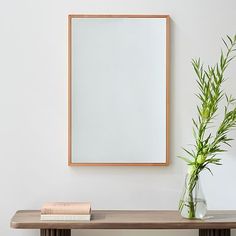 a wooden table topped with a vase filled with green plants next to a framed mirror