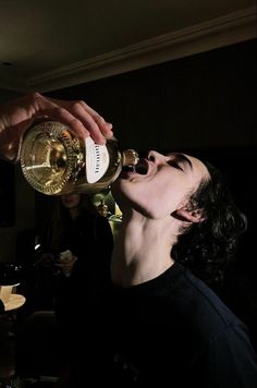 a man is drinking from a bottle while another person looks on in the dark behind him