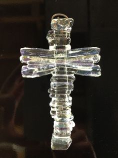 a glass crucifix is hanging on a black surface with the reflection of it's cross