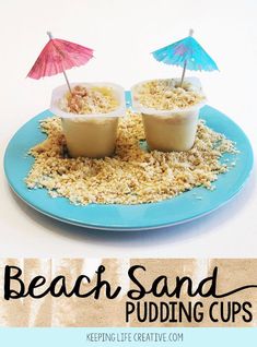 two cups filled with pudding on top of a blue plate covered in sand and an umbrella