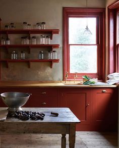 a kitchen with red cabinets and shelves filled with glassware on top of a wooden table